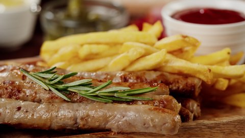 Bowl with sauce and smoked sausages with fried potatoes rotating close-up. Traditional German cuisine, bratwursts and potatoes on the table. Composition of cooked national Czech Food.