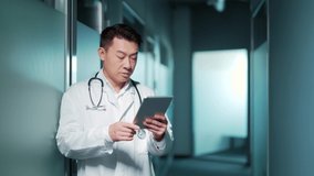 Asian male doctor advise patient remotely using digital tablet. Communicates online talks on video call standing in a modern hospital clinic. Male doctor therapist prescribes treatment. Telemedicine