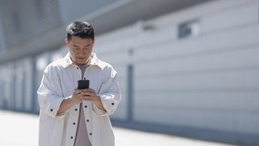 Young Asian handsome man smiling while reading messages on a smartphone, on a walk around the city