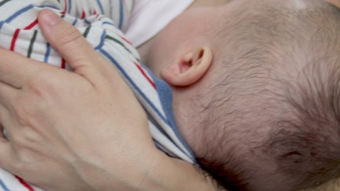 a yound mother is feeding her new born child with brest. brestfeeding concept. baby in striped bodysuit. mom is swinging the child. close-up video. lactation, nursing. hungry baby. 