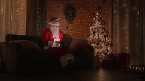 Santa Claus working on laptop sends letters with wishes or congratulations by email for Christmas or New Year. Santa communicates on social networks with children around world.