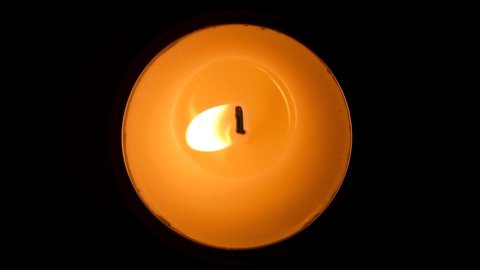 Candle flickering in the dark. Top view. White round candle burning on the dark background. Slow motion video.