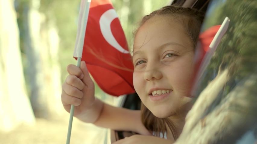 Slow Motion:Beautiful little girl waving Turkish flag out of a car window.Travel Concept. Little girl coming out of the car window smiling and waving the Turkish flag. Celebration concept.  Royalty-Free Stock Footage #1084291078