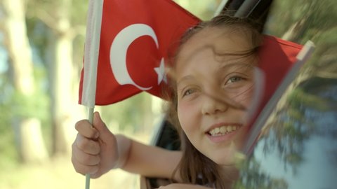 Slow Motion:Beautiful little girl waving Turkish flag out of a car window.Travel Concept. Little girl coming out of the car window smiling and waving the Turkish flag. Celebration concept. 