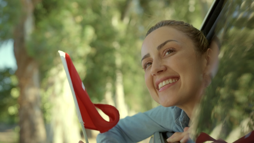 Slow Motion: Beautiful young woman waving Turkish flag from a car window.Travel Concept. Young woman coming out of car window smiling and waving Turkish flag. Celebration concept.  Royalty-Free Stock Footage #1084291303