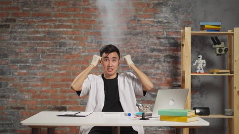 Overworked Asian scientist in robe with steam pillar above head shakes fists crazy of bad experiment at workplace in scientific laboratory