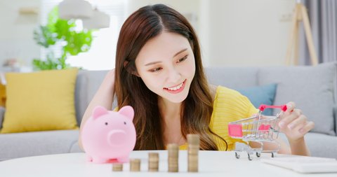 inflation concept - asian woman woman plays small shopping cart with coins and piggy bank at home