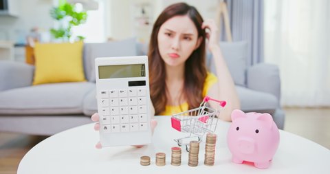 inflation concept - worried asian woman woman shows calculator with coins and piggy bank at home