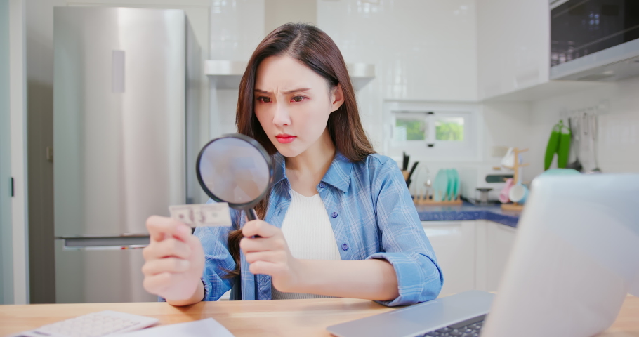 inflation concept - worried asian woman find money is getting smaller by magnifier at kitchen