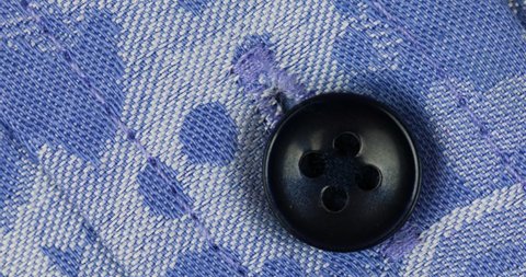 Black Plastic Sew Button Attach On Blue Woven-Patterned Fabric. Closeup, Rotate