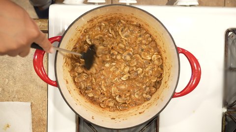 Adding corn starch and broth to sauteed mushrooms in a pot on the stove to thicken the soup - overhead view WILD RICE SERIES