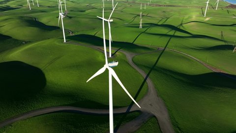 Orbiting around Wind Turbine spinning in slow motion against green hills at Wind Turbine Farm, Northern California