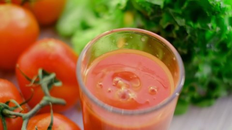 slow motion drops of tomato juice dripping into a glass of juice. tomato juice with sprig of tomatoes on background. Tomato juice is poured into a glass.