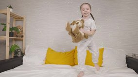 cheerful little girl jumping on the bed with a teddy bear, children's games and entertainment at home, outdoor outdoor activities on a weekend, favorite toy of a laughing kid in bed, happy family - Powered by Shutterstock - Get 15% off with code: PIKWIZARD15