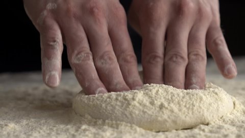 Hands crushing the dough. Chef preparing pizza dough. Dough and flour lying on the table against the background of a brick oven with fire. Pizzaiolo preparing dough with his hands. Slow motion