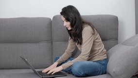 Stock video of freelancer writer typing text on notebook computer while sitting on couch at home during lockdown. Beautiful young woman in 30s working on laptop in living room