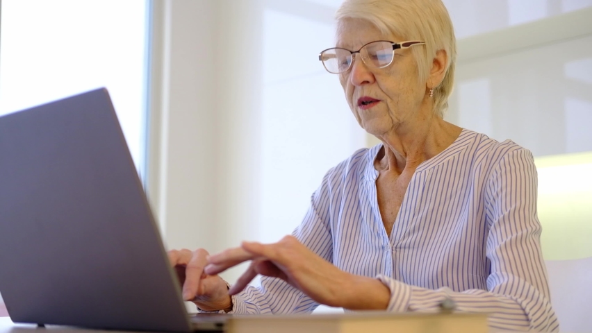Senior mature older woman working on laptop at kitchen home in office. lady watching business training, online webinar on computer. remote working social distance learning from home. 60s woman  Royalty-Free Stock Footage #1084305571