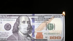One hundred usd dollar bill with protective medical mask on Benjamin Franklin portrait burning from fire. Economic Crisis during Covid-19 Pandemic concept. 100 dollar banknote. 4k high quality video