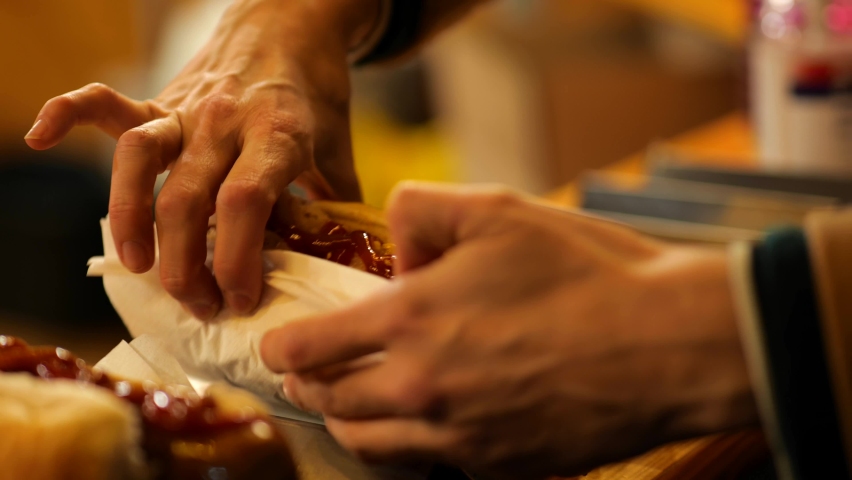 A woman picks up and eats a sausage in a bun with sauerkraut and tomato sauce. Outdoor street food at a Christmas market