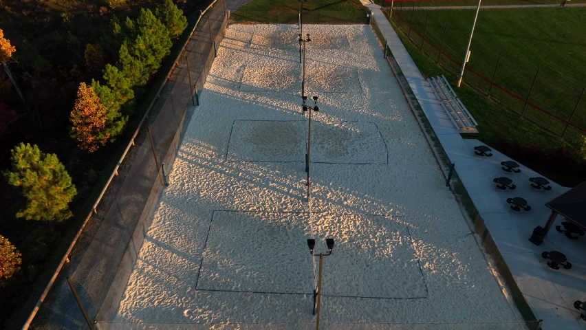 Aerial tilt up reveals outdoor sand volleyball courts during golden hour light. No people. Beach volleyball theme.