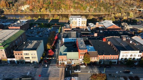 Aerial establishing shot of restored storefront businesses in small town America. Golden hour light during colorful autumn foliage. River in distance.