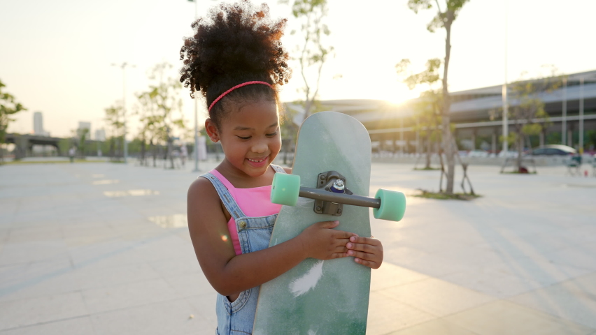 4K Portrait of Smiling little African child girl kid skateboarding at the park. Cute preschool girl enjoy and having fun outdoor lifestyle practicing extreme sport longboard skating on summer vacation