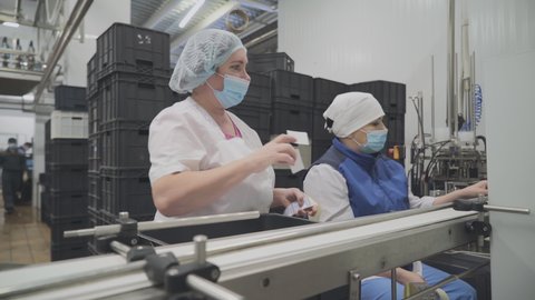 Two Female Operators are Sticking Labels. Putting the dairy food Products in black Container and Placing it on a Conveyor Belt . Manufacturing of Dairy food Based Goods. Dairy Food Packaging Process.