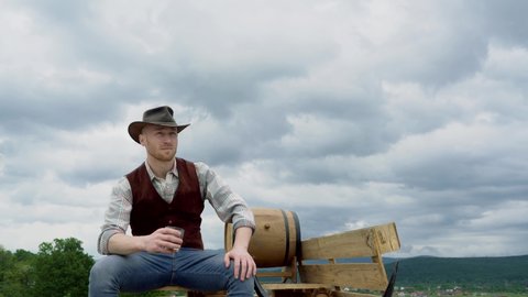 Portrait of farmer or cowboy drink whiskey outdoor. American cowboy man. Handsome brutal western guy.