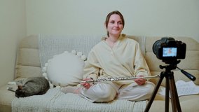 Happy woman musician with flute looking at video camera at home on sofa in living room