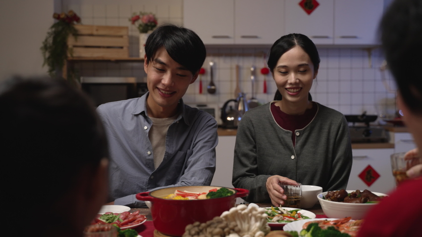 selective focus of happy young asian couple drinking toast with tea to their family at chinese chinese lunar new year reunion dinner at home. chinese text translation: fortune Royalty-Free Stock Footage #1084321261