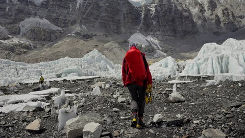 Alpinist with red backpack walk on rocky path along glacial to Everest Base Camp