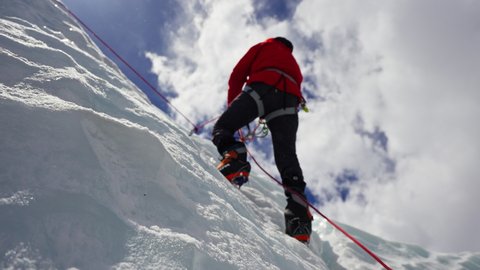 Alpinist equipped with red crampon ascending over white frozen slope in sunshine