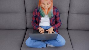 Freelancer girl with dyed hair working from home on lockdown. Young woman in late 20s with colored hair typing text on laptop computer in living room. Stock video clip of free lancer filmed in 4K