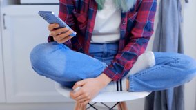 Young girl browsing news feed on mobile phone. Teenager with colored hair wearing casual clothes scrolling social media app on mobile phone. Royalty free stock video in 4k