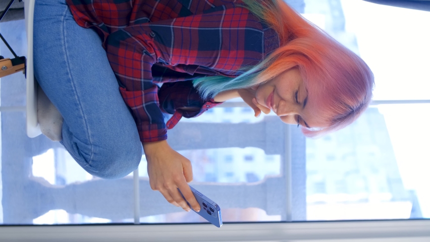 Young girl with dyed hair using mobile phone. Vertical stock video of female browsing news feed on social media app in modern smartphone. Royalty free 4K footage of young woman using cellphone | Shutterstock HD Video #1084329124