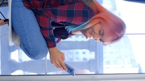 Young girl with dyed hair using mobile phone. Vertical stock video of female browsing news feed on social media app in modern smartphone. Royalty free 4K footage of young woman using cellphone