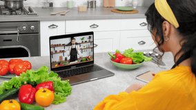 Man food blogger in computer screen tells teaches housewife online video call webcam chat laptop. Woman in home kitchen study watch remote culinary webinar listen chef teacher, writes in notebook