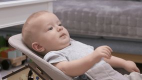 Dad handing mobile device to child to entertain him, baby boy using tablet sitting on rocking chair in living room. High quality 4k footage