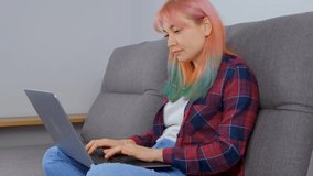 Focused freelancer girl with dyed hair working from home on lockdown. Individual young woman with colored rainbow hair doing distant work on laptop computer. 4K stock video clip