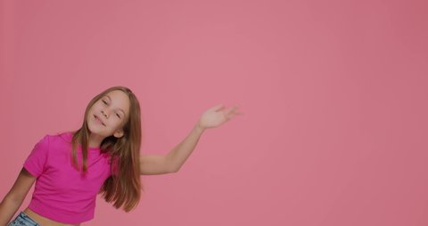 Smiling girl child greeting, wave hand say hello or bye to subscribers, peek out on pink background with copy space