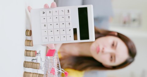 inflation concept - vertical video of worried asian woman woman shows calculator with coins and piggy bank at home
