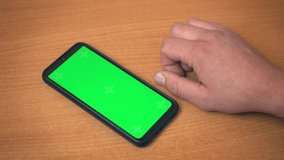 Top view of male hands holding mobile phone with green mock up screen. Caucasian man using modern smartphone at workplace. Surfing Internet Watching Content Videos Blogs Tapping on Center Screen 4k