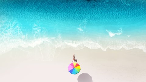 Beautiful young woman at luxury hotel resort celebrating summer vacation under colorful sun umbrella. Aerial view of sand beach. Girl enjoying sunny day on travel holiday  on empty white sand beach
