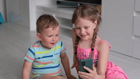 Brother and sister watch cartoons on the phone and laugh. Children hold the phone and talk online via video link.
