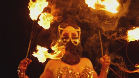 Young woman dancing performing cool and dangerous fire show and doing many tricks with fire . Dressed in black with mask closed half of face . Burning iron fire wings at night. Asian , Arabian culture