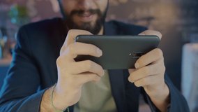Close-up of happy Middle Eastern employee playing video game using smartphone relaxing at work at night. People and entertainment concept.