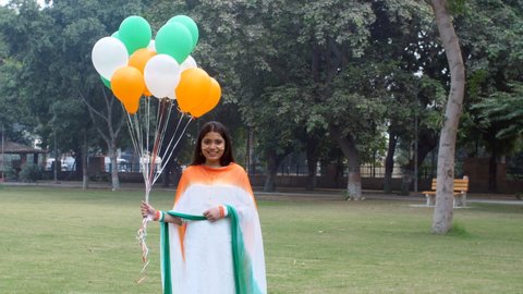 A cheerful girl wearing a tricolor Dupatta with balloons on Republic Day celebrations. A young girl wearing tricolor armbands and a sketch of the National Flag on her face - patriotism, Independence