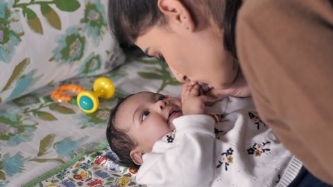Young Indian mother playing with her baby - Baby growth, learning, baby development, childhood. A happy Indian mother kissing and hugging her newborn baby girl - family bonding, happy parenting