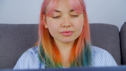 Confused freelancer girl with dyed hair communicating with clients online working from home on lockdown. Stock 4K video of individual young woman with colored hair works free lance on laptop computer