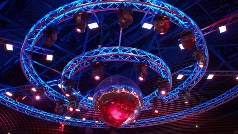 night disco club with neon blue violet red light, disco mirror ball and bright floodlight with round metal frame luminous construction